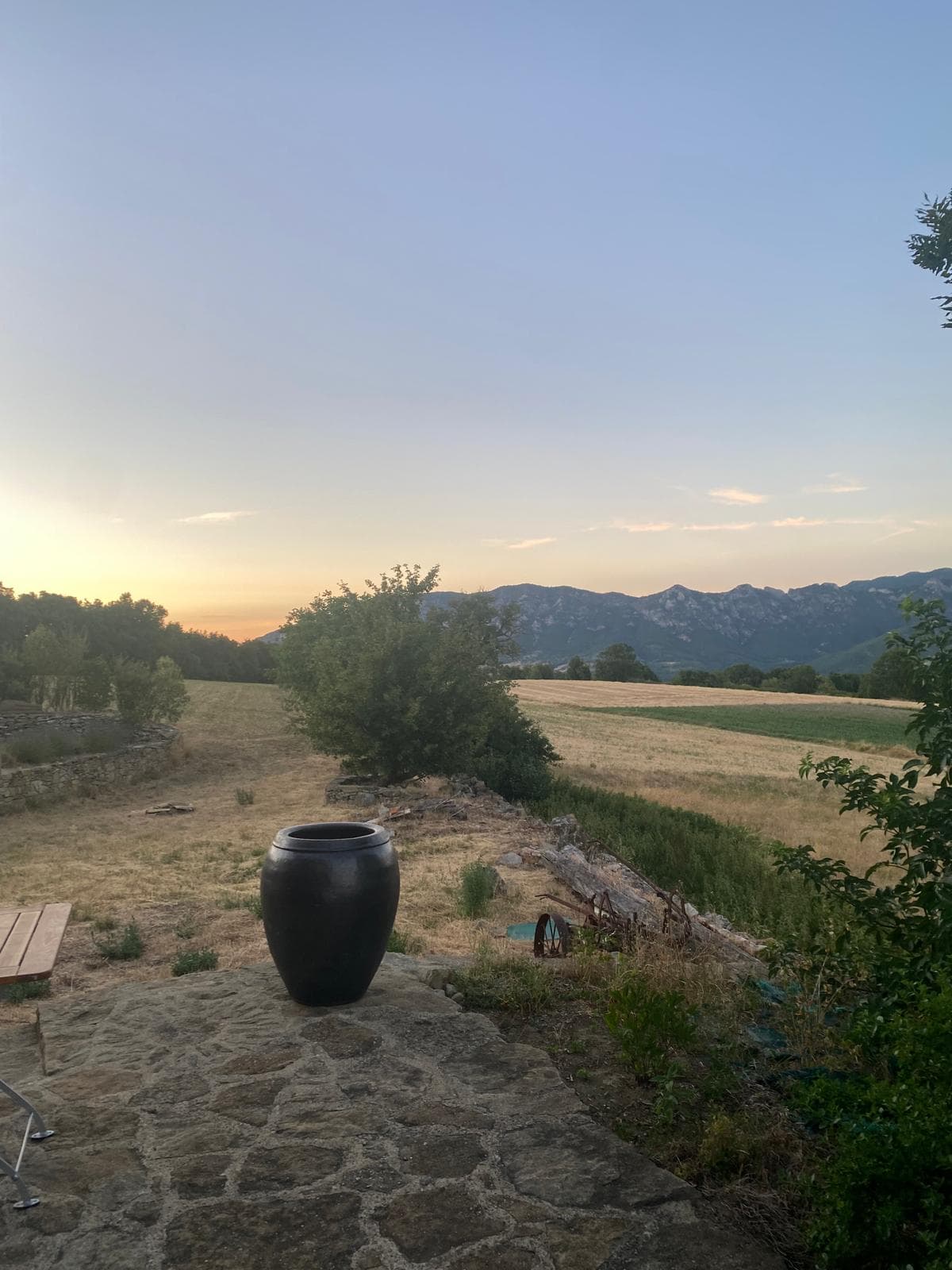 La terrasse en pierre et sa grande jarre noire, face aux montagnes de la Drôme au couchant
