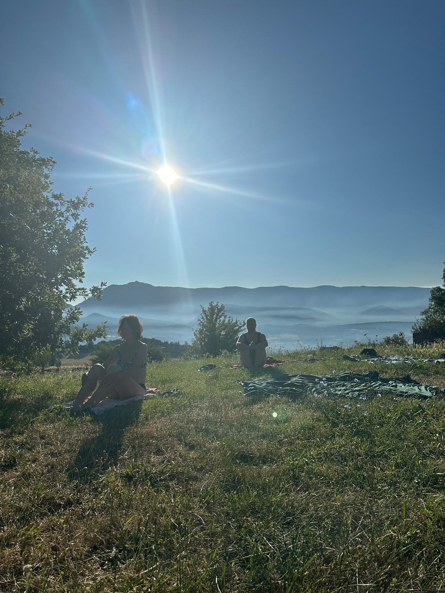 Des participants assis dans l'herbe face aux montagnes au soleil du matin