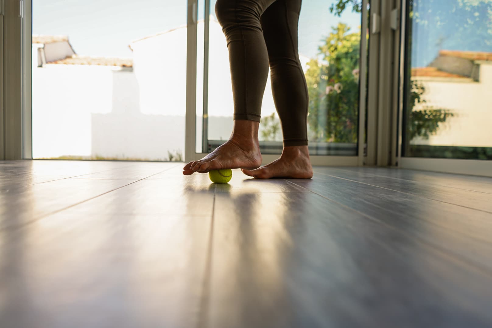 Pied roulant une balle de massage au sol, face à une baie vitrée