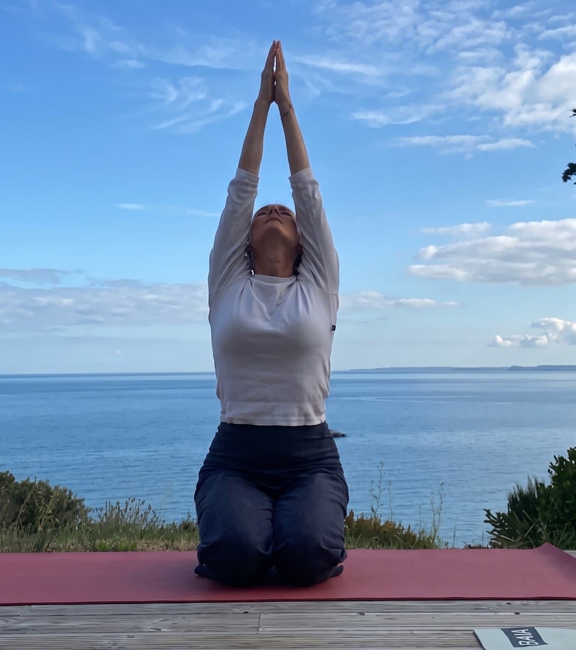 Pratique du matin sur la terrasse en bois, bras levés face à la mer